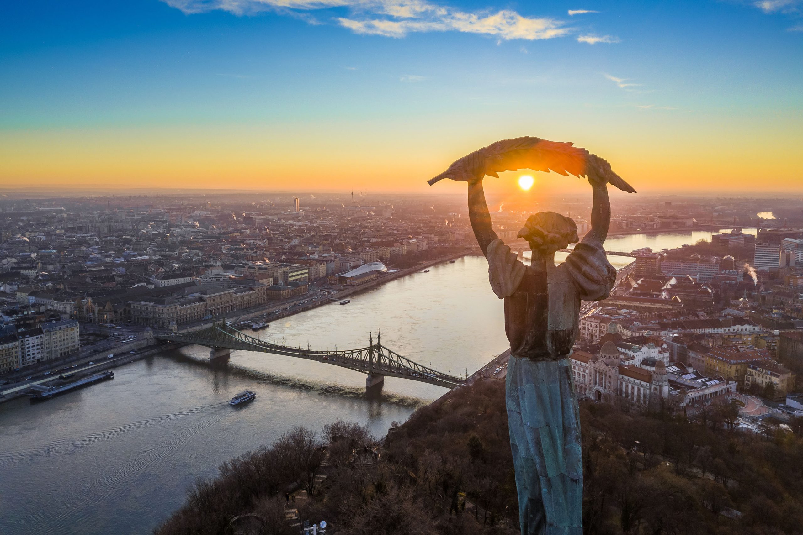 Aerial view of Budapest at sunrise, with the Liberty Statue overlooking the Danube River and Liberty Bridge.